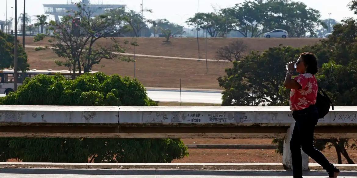 Seca e alta temperatura em Brasília. Pessoa com copo de água passa pelo Setor de Diversões Sul (Bruno Peres/Agência Brasil)